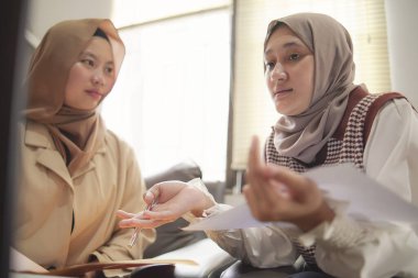 Modern bir ofis, profesyonel işbirliği ve dijital yaşam tarzında dizüstü bilgisayarda birlikte çalışan iki güzel Asyalı Müslüman iş kadını.