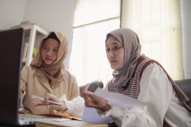 Modern bir ofis, profesyonel işbirliği ve dijital yaşam tarzında dizüstü bilgisayarda birlikte çalışan iki güzel Asyalı Müslüman iş kadını.