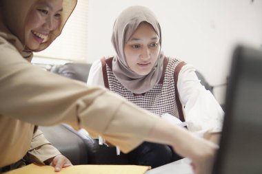 Modern bir ofis, profesyonel işbirliği ve dijital yaşam tarzında dizüstü bilgisayarda birlikte çalışan iki güzel Asyalı Müslüman iş kadını.