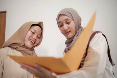 İki güzel Asyalı genç Müslüman iş kadını modern bir ofiste çalışırken gülümseyen bir klasörde belgeleri tartışıyor.