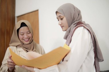 İki güzel Asyalı genç Müslüman iş kadını modern bir ofiste çalışırken gülümseyen bir klasörde belgeleri tartışıyor.