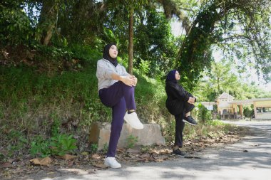 Yeşil bir parkta güneşli bir günde, tesettür takan ve ısınan iki genç Müslüman kadın. Sağlıklı yaşam tarzı, arkadaşlık ve doğal ışık ile uygunluk kavramı