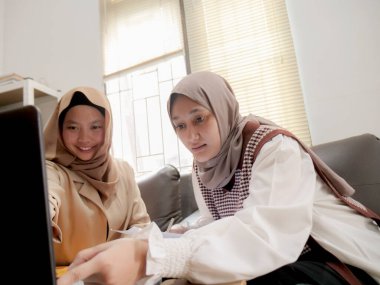 Modern bir ofis, profesyonel işbirliği ve dijital yaşam tarzında dizüstü bilgisayarda birlikte çalışan iki güzel Asyalı Müslüman iş kadını.