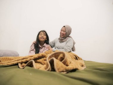 Güzel Asyalı tesettürlü Müslüman anne genç kızını yatakta, sabah rutininde ve annelik kavramında uyandırıyor.