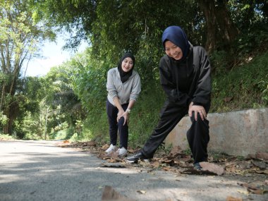 Yeşil bir parkta güneşli bir günde, tesettür takan ve ısınan iki genç Müslüman kadın. Sağlıklı yaşam tarzı, arkadaşlık ve doğal ışık ile uygunluk kavramı