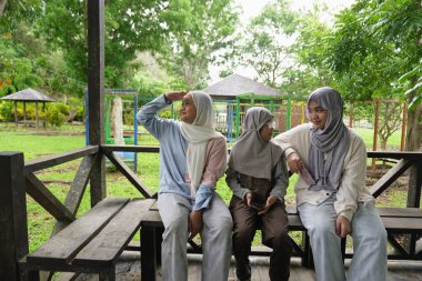 Üç mutlu gülümseyen Asyalı genç kız sabahın köründe yemyeşil bir bahçede geleneksel ahşap bir çardakta birlikte oturuyorlar.