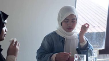 İki güzel Asyalı Müslüman genç kız bir kafede öğle yemeği yiyor. Barışçıl bir ortamda konuşup gülüyorlar.