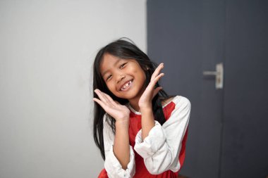 Küçük sevimli Asyalı kız elleriyle gülümsüyor, mutlu çocuk neşeli bir ifade ve beyaz dişler gösteriyor, saf mutluluk kavramı, çocukluk cazibesi ve diş sağlığı.