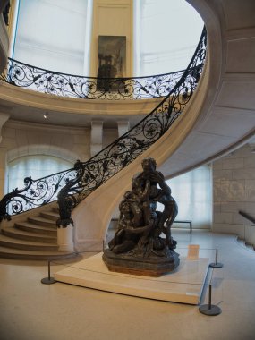 Müze İçi Spiral Merdiven ve Heykel - Paris müzesindeki bir bronz heykelin etrafında dönen işlenmiş demirle döşenmiş büyük sarmal bir merdivenin zarif iç çekimi.