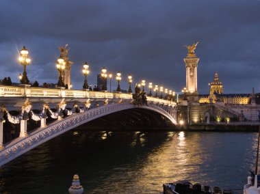 Pont Alexandre III Gece Işıklandırıldı - Görkemli Pont Alexandre III köprüsü Paris 'teki Seine Nehri' ne yansıyan altın heykeller ve sokak lambalarıyla karanlık, bulutlu bir gökyüzüne aydınlandı.