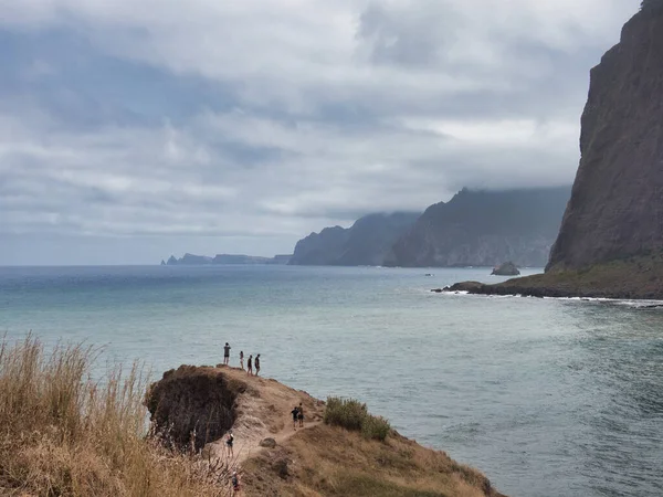 Turistli Madeira Sahil Hattı Vista - Madeira 'nın yüksek uçurumları, bulutları ve küçük turist figürleriyle dolu engebeli kıyı şeridine dramatik bir okyanus manzarası.