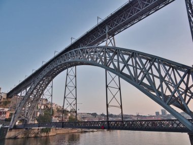 Dom Lus I Bridge ve Porto Skyline Sunset 'te - Douro Nehri boyunca uzanan ikonik metal kemer köprüsünün yüksek açılı görüntüsü, yayalar ve tarihi Porto silueti ve yumuşak akşam ışığında anıtlar.