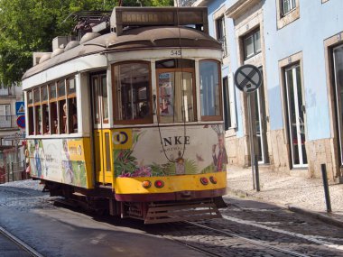 Klasik Reklam Tramvayı Lizbon Cobblestone Hill 'e tırmanıyor. Güneşli bir günde dik bir kaldırım taşına tırmanan bir içki markası için renkli yan reklamları olan klasik bir Lizbon tramvayı..