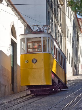 Dik Lizbon Tepesi 'ndeki Glria Funicular - Sarı Elevador da Glria klasik tramvayı Lizbon dik Bairro Alto tepesine tırmanıyor kaldırım taşı bir sokakta, pembe tarihi bir binanın yanında.