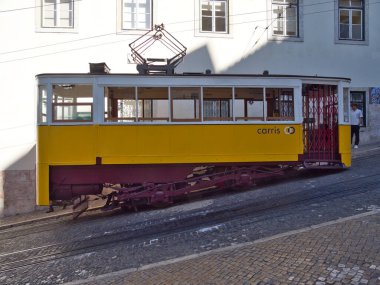 Dik Lizbon Tepesi 'ndeki Glria Funicular - Sarı Elevador da Glria klasik tramvayı Lizbon dik Bairro Alto tepesine tırmanıyor kaldırım taşı bir sokakta, pembe tarihi bir binanın yanında.