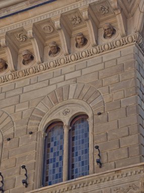 Rönesans Penceresi ve Taş Cephesi 'ndeki büstler - Tarihi Floransa Sarayı' ndaki bir heykel kafasının heykeli ve kırsal taş işçiliğiyle çerçevelenmiş kareli bir pencereye yakın plan.
