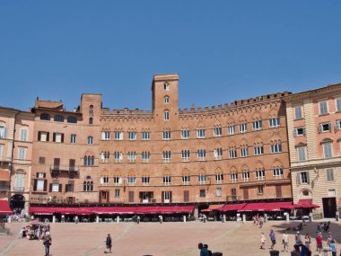 Siena 'daki Piazza del Campo ve Palazzo Pubblico - Tuscany' de güneşli bir günde, Palazzo Pubblico 'nun eğri, orta çağ, kırmızı tuğlalı cephesi ve kalabalık Piazza del Campo' nun geniş yatay manzarası.
