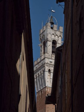 Torre del Mangia Narrow Siena Alley tarafından çerçevelenmiştir - Beyaz taşın dramatik, düşey alçak açılı görüntüsü ve Torre del Mangia keskin çerçeveli Ortaçağ 'ın karanlık, gölgeli duvarları Siena' da.