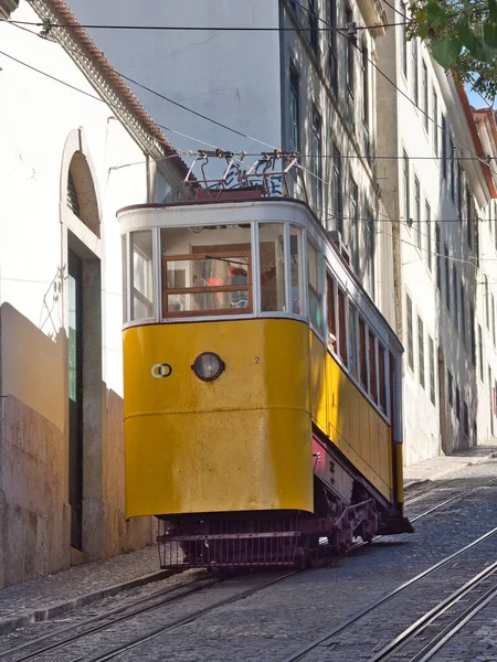 Dik Lizbon Tepesi 'ndeki Glria Funicular - Sarı Elevador da Glria klasik tramvayı Lizbon dik Bairro Alto tepesine tırmanıyor kaldırım taşı bir sokakta, pembe tarihi bir binanın yanında.