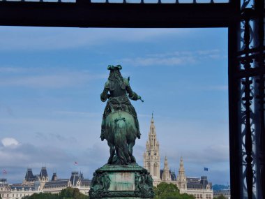 Viyana Belediyesi ile birlikte çerçevelenmiş Binicilik Heykeli - Uzaklarda Neo-Gotik Rathaus kulesi olan karanlık bir kemer tarafından çerçevelenmiş tarihi bronz süvari heykeli.