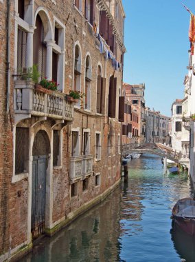 Klasik Venedik Tuğla Kanalı Balkon ve Köprü - dar, tarihi Venedik kanalı kırmızı tuğlalı binalar, gotik kemerli pencereler, taş balkonlar ve uzakta küçük bir köprü.