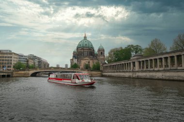Berlin Katedrali ve Spree Nehri Tekne Turu - Spree Nehri üzerinde bir turist teknesi, Berlin Katedrali 'ni (Berliner Dom) dramatik ve bulutlu bir gökyüzü altında güzel güneş ışınlarıyla geçer..