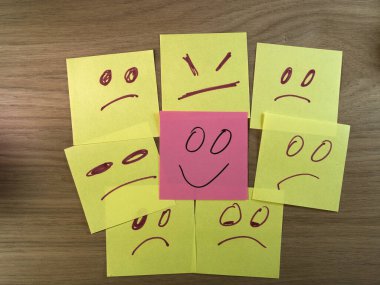 Üzgün Yüzler Arasındaki Mutlu Yüz, Kızgın Yüzler - Mutlu yüzle çevrili pembe yapışkan bir nota, üzgün, kızgın yüzler tahtada. Duygular, akıl sağlığı, bireysellik, kontrast.