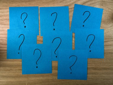 Birçok Mavi Soru Tahtadaki İşaretleri - Elle çizilmiş soru işaretli yedi mavi notlar ahşap masaya saçılmış, karmaşayı, sorgulamayı ve problem çözmeyi simgeliyor.