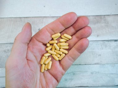 Avuç içlerindeki ilaç kapsülleri sayısız sarı hap kapsülüyle dolu yetişkin bir elin görüntüsü. Sağlık, ilaç, reçete ve terapi konuları için ideal.