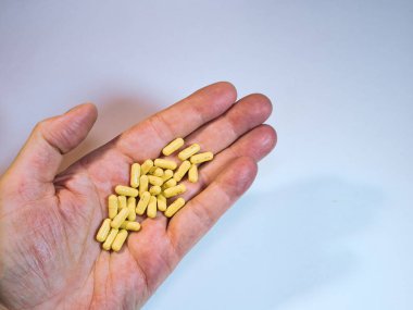 El ele tutuşan sarı haplar - Bir avuç sarı ilaç kapsülünü ya da vitamini, sade beyaz bir zemin üzerinde tutarak, sağlık, ilaç ya da tedaviyi sembolize eden insan elinin yakın çekimi.