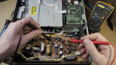Çokölçer ile Elektronik Onarım ve Bakım Bir DVD oynatıcısının veya benzer bir cihazın devre kartındaki voltajı kontrol eden bir teknisyenin elleri.