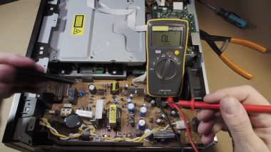 Çokölçer ile Elektronik Onarım ve Bakım Bir DVD oynatıcısının veya benzer bir cihazın devre kartındaki voltajı kontrol eden bir teknisyenin elleri.