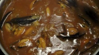 Domates sosunda pişiren midyeler, üstte karıştırma; yakın çekim, zengin, kaynayan bir domates veya paslanmaz çelik bir tencerede köri sosu içinde kaynayan midyeler. Bir kaşık lezzeti karıştırır