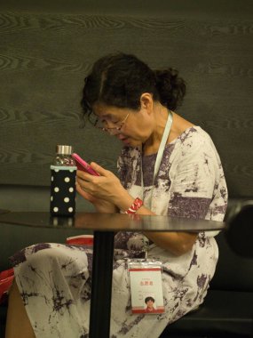 Şangay-Şangay-Çin-14 Ağustos 2018, Çin Sanat Müzesi 'nde (Şangay, Çin) bir gönüllü mola sırasında bir masada oturuyor, pembe bir akıllı telefon tutuyor ve konuşurken işaret veriyor..