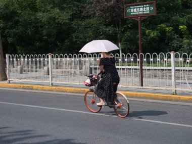 Pekin-Pekin-Çin-9 Ağustos 2018, Çin 'de Doğu Huancheng Yolu' nda (Kuzey Bölümü) bisiklet sürerken bir kadın kendini güneş ışığından korur..