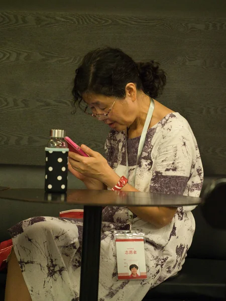 Şangay-Şangay-Çin-14 Ağustos 2018, Çin Sanat Müzesi 'nde (Şangay, Çin) bir gönüllü mola sırasında bir masada oturuyor, pembe bir akıllı telefon tutuyor ve konuşurken işaret veriyor..