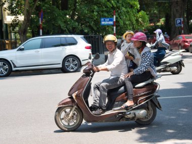 Hanoi-Vietnam-9 Ağustos 2019 üç kişilik Vietnamlı bir aile Honda scooter ile Ph Bnh Tin Hong 'da park halindeki bir BMW SUV' nin yanından geçiyor..