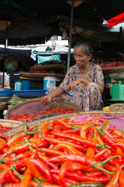 HANOI-Vietnam-14 Ağustos 2019, Güneydoğu Asya 'daki hareketli bir markette geleneksel sepetlerde canlı kırmızı ve turuncu biberler satan yaşlı bir kadın görülüyor..