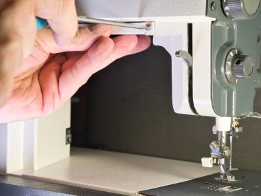 Vintage dikiş makinesini ayarlamak; eski, klasik bir dikiş makinesini kuran veya tamir eden birinin elinin yakın plan çekimi. ÇEVİRİ becerilerini vurgulayarak mekanizma, iğne ve basınçlı ayak alanına odaklan.