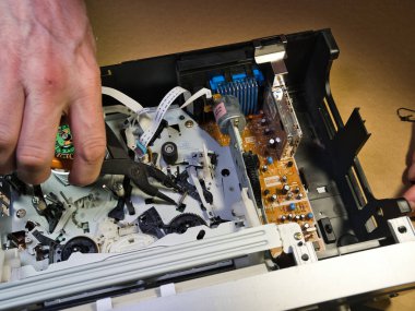 VHS bantlı VCR Onarım ve Bakım; Parçalanmış bir VCR mekanizmasını tamir eden bir teknisyenin genel görünümü. Dahili devre kartları ve test araçları ile çevrili bir VHS bandı yüklendi.