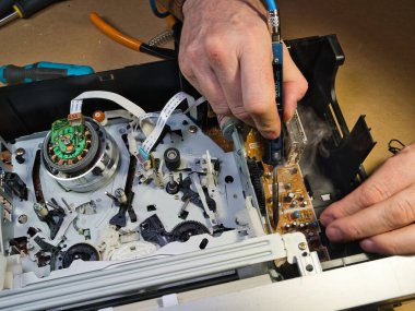 VHS bantlı VCR Onarım ve Bakım; Parçalanmış bir VCR mekanizmasını tamir eden bir teknisyenin genel görünümü. Dahili devre kartları ve test araçları ile çevrili bir VHS bandı yüklendi.
