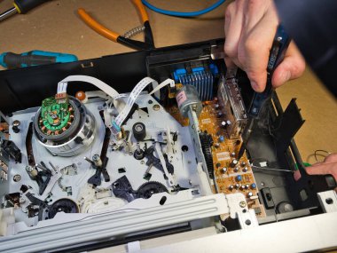 VHS bantlı VCR Onarım ve Bakım; Parçalanmış bir VCR mekanizmasını tamir eden bir teknisyenin genel görünümü. Dahili devre kartları ve test araçları ile çevrili bir VHS bandı yüklendi.