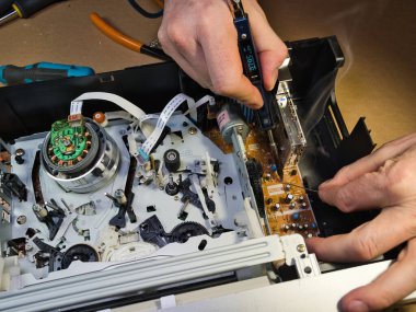 VHS bantlı VCR Onarım ve Bakım; Parçalanmış bir VCR mekanizmasını tamir eden bir teknisyenin genel görünümü. Dahili devre kartları ve test araçları ile çevrili bir VHS bandı yüklendi.
