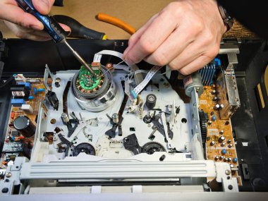VHS bantlı VCR Onarım ve Bakım; Parçalanmış bir VCR mekanizmasını tamir eden bir teknisyenin genel görünümü. Dahili devre kartları ve test araçları ile çevrili bir VHS bandı yüklendi.