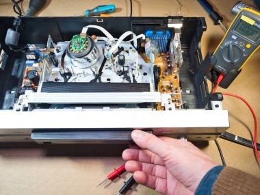 VHS bantlı VCR Onarım ve Bakım; Parçalanmış bir VCR mekanizmasını tamir eden bir teknisyenin genel görünümü. Dahili devre kartları ve test araçları ile çevrili bir VHS bandı yüklendi.