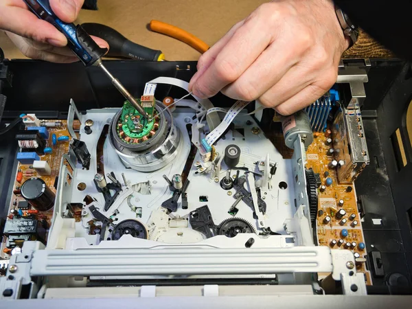 VHS bantlı VCR Onarım ve Bakım; Parçalanmış bir VCR mekanizmasını tamir eden bir teknisyenin genel görünümü. Dahili devre kartları ve test araçları ile çevrili bir VHS bandı yüklendi.