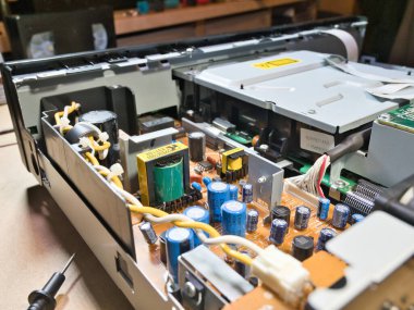 Eller Elektronik Devre Tahtasını Çokölçer ile Test Ediyor; Açık bir DVD / Blu-ray oynatıcı veya benzeri bir aygıt içindeki kompleks elektronik devreleri tanımlamak veya onarmak için çokölçer kullanan teknisyenlerin ellerinin yakın çekimi.