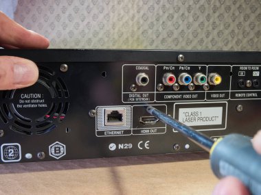 AV elektronik aygıt bağlantılarının teknik onarımı; HDMI, Ethernet, Bileşik Video ve Eaksiyel portların yer aldığı bir elektronik cihazın arka panelini açmak veya onarmak için bir tornavida kullanan Hand. DIY kurulumu ve bakımı.