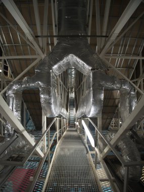 Endüstriyel Havalandırma Kanalları ve Bakım Platformu; yalıtımlı HVAC havalandırma kanalı görüntüsü ve modern endüstriyel veya ticari bir binanın tavan yapısında metal bakım platformu.