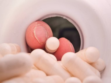 Plastik şişeden beyaz kapsülleri alan el, ilaç dozajını, tüketimini veya bağımlılığı gösteren beyaz ilaç kapsüllerini alan elin aşırı yakın plan çekimi..